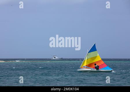 ORANJESTAD, ARUBA - MARCH 27, 2022: Young man sailing small sunfish dinghy with colorful sail along the coast at Surfside beach in Oranjestad on Aruba Stock Photo