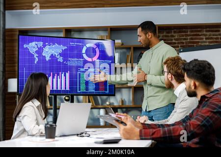 Motivated african american businessman having business meeting with managers, negotiating, using presentation tv with statistics, charts, big data Stock Photo