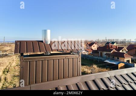 Chimney on house roof top covered with metallic shingles under construction. Tiled covering of building. Real estate development Stock Photo