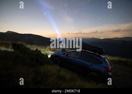 Silhouette of man at offroad car with head flashlight on background of very beautiful night starry sky after sunset. Freedom and travel by car concept Stock Photo