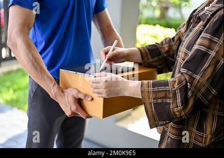 Close up view of Delivery man in blue uniform have his customer sign on tablet for the package. delivery service concept Stock Photo