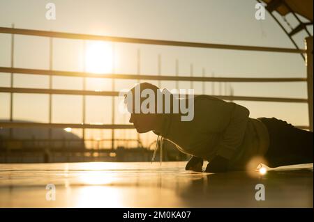 Young caucasian man doing push-ups in the boxing ring outdoors at sunset. Stock Photo