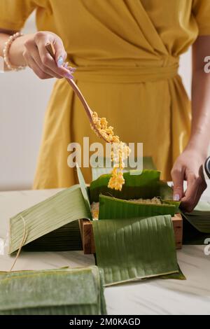 Housewife adding mung beans in mold covered with banana leaves Stock Photo