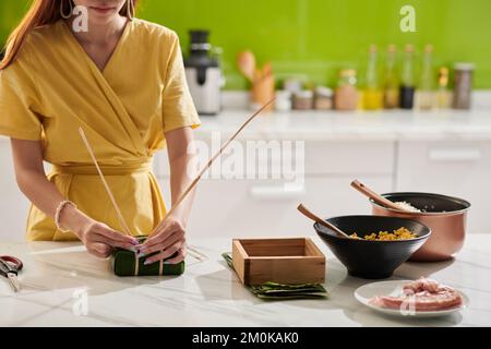 Closeup image of woman packing rice cake in banana leaves for Tet celebration Stock Photo