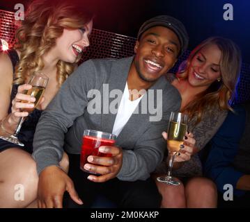 Hes a hit with the ladies. A handsome young African-American man sitting in a nightclub with two beautiful caucasian women next to him. Stock Photo
