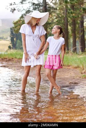 This is fun, isnt it. A cute little girl holding mother by the hand while standing in a wilderness stream. Stock Photo