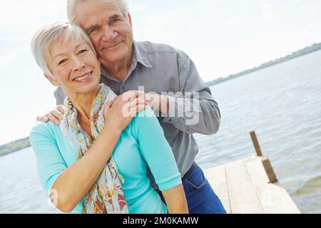 Timeless love. A mature husband and wife looking at the camera and smiling while standing on a jetty by the lake. Stock Photo