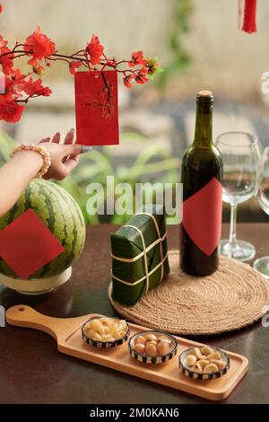 Hand of woman hanging greeting card on blooming peach branch on table served for Tet celebration Stock Photo