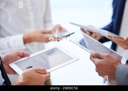 Unknown group of diverse businesspeople using technology in office huddle. Team of colleagues standing together, using bluetooth to sync data and Stock Photo