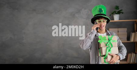 St. patrick's day sale, festive online shopping, young man in leprechaun hat holding delivery boxes and talking on mobile phone. Banner Stock Photo