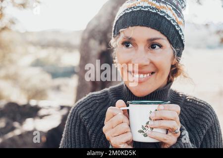 Face portrait of cheerful middle age pretty woman drinking cup of tea or coffee in outdoor leisure activity alone. Smiling lady looking on side. Natur Stock Photo
