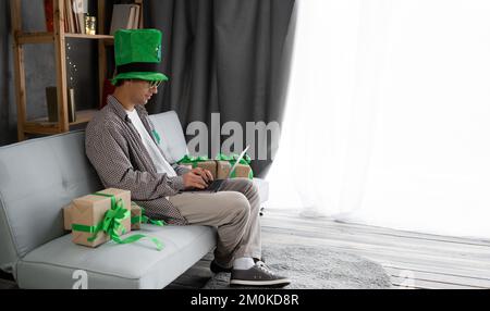 Happy guy in leprechaun hat using laptop, ordering St.Patrick's day gifts on web, shopping for St.Patrick's Day presents online from home. Arabic man Stock Photo