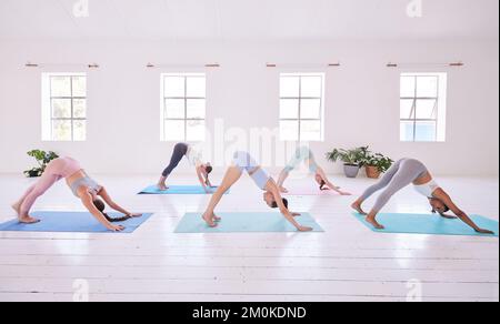 Group of women in downward dog pose. Young women practice yoga together in a class. Group of flexible women stretching together in yoga class Stock Photo