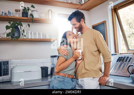 Happy young interracial couple spending time together at home. Young woman enjoying her morning coffee while boyfriend puts his arms around her. Young Stock Photo