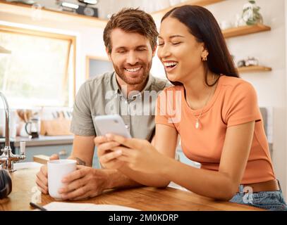Young content interracial couple using a phone together at home. Happy caucasian boyfriend and mixed race girlfriend laughing while using social media Stock Photo