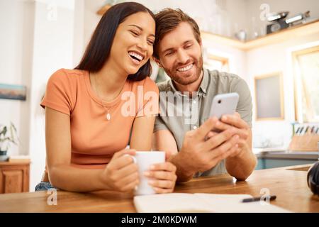 Young cheerful interracial couple using a phone together at home. Happy caucasian boyfriend and mixed race girlfriend laughing while using social Stock Photo