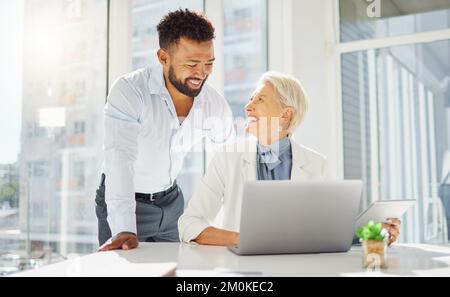 Two happy diverse colleagues working together on a laptop and digital tablet device in an office boardroom. Young mixed race businessman meeting with Stock Photo