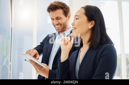 Confident asian businesswoman thinking of ideas with her hand on her chin while planning a project with a caucasian businessman using a digital tablet Stock Photo