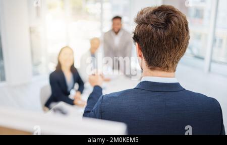 High angle of one young caucasian businessman from the back using a whiteboard to write notes while leading a presentation with his colleagues during Stock Photo