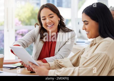 Team of two smiling business women using a digital tablet for a brainstorm meeting in the office. Happy confident ethnic professionals using Stock Photo