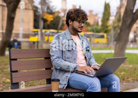 Indian sad and angry businessman in formal wear sitting on bench with laptop Stock Photo