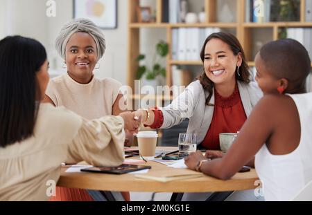 Team of smiling diverse business women shaking hands in office after meeting in boardroom. Group of happy professionals and colleagues using handshake Stock Photo