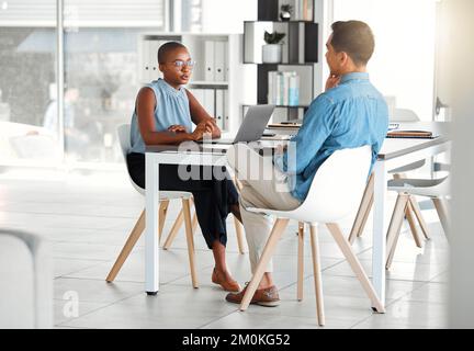 Two businesspeople having a meeting together in an office at work. Young african american businesswoman talking to an asian businessman while working Stock Photo