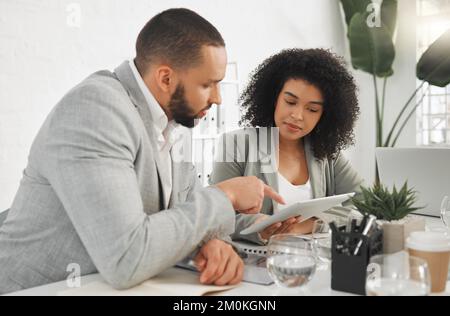 Two mixed race businesspeople working on a digital tablet in a meeting together at work. Business professionals using technology in an office Stock Photo