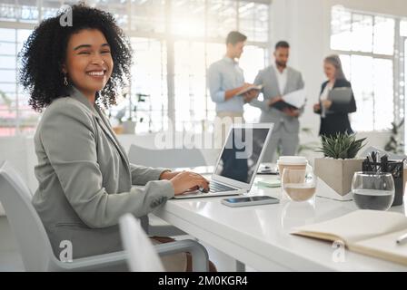 Portrait of a cheerful mixed race businesswoman working on a laptop at work. Happy hispanic female businessperson with a curly afro typing en email on Stock Photo