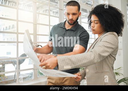 Two colleagues holding a blueprint. Two architects working on a building project. Corporate designers planning a project together. Young coworkers Stock Photo