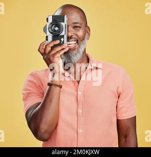 One happy African American man standing against a yellow background in a studio and taking pictures on a camera. Confident cheerful black man holding Stock Photo