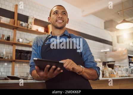 Barista dreaming while ordering stock on digital tablet. Mixed race businessman using wireless device in cafe kitchen. Business owner thinking while Stock Photo