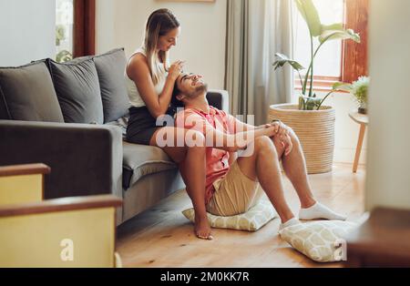 Loving young caucasian couple sitting together at home spending time and happy to be together. Happy young woman sitting on couch while her boyfriend Stock Photo