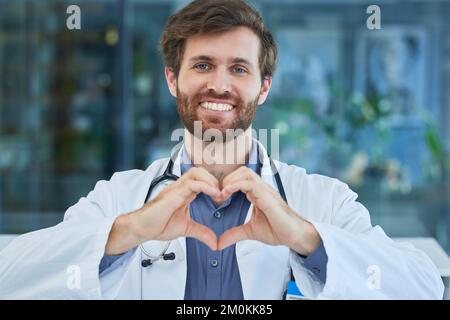 Man, doctor and heart sign with smile, support and healthcare in hospital. Medical professional, male and hand gesture for shape, love or solidarity Stock Photo