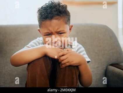 One mixed race little boy crying on the sofa at home. African American child suffering from PTSD after being abused and neglected. Grieving little Stock Photo