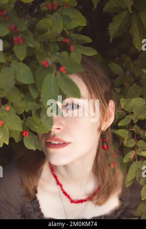 Close up woman peeking through winterberry leaves portrait picture Stock Photo