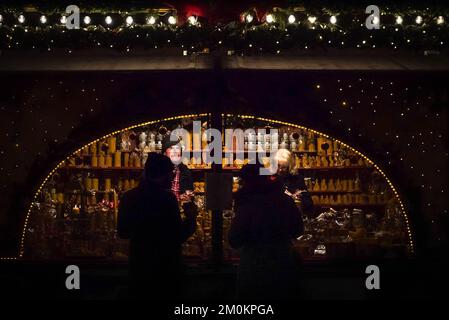 Two silhouettes of the customers stands near lighted kiosk at a Christmas market in Munich, Germany at night with two sellers inside of the counter. Stock Photo