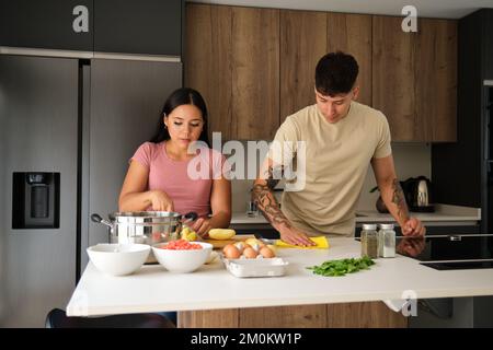 Two young latin people peeling potatoes and cleaning kitchen counter at kitchen. Stock Photo