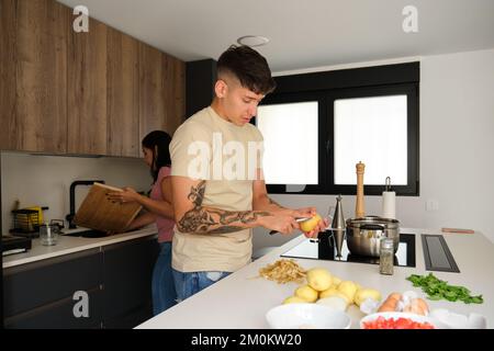 Two young latin people peeling potatoes and washing chopping board at kitchen. Stock Photo