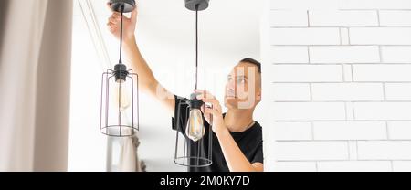 Worker repairing lamp on stretch ceiling indoors Stock Photo