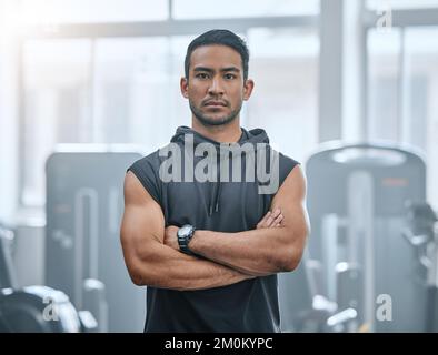 Portrait of one serious asian trainer alone in gym. Handsome focused coach standing with arms crossed after workout in health club. Young confident Stock Photo