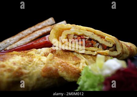 Omelet with vegetables, sausages, herbs and toast on a black background Stock Photo