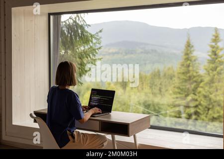 Woman works on laptop remotely in house on nature Stock Photo