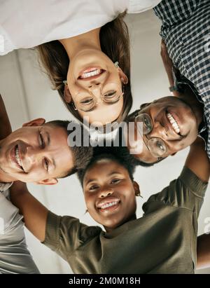 Team of creatives huddled together in unity. Happy diverse business team standing in circle embracing each other and smiling, from below Stock Photo