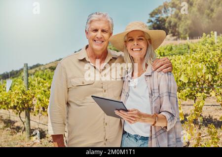 Portrait of two happy senior farmers standing and using digital tablet on their vineyard. Smiling elderly man and woman bonding together on wine farm Stock Photo