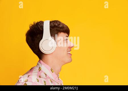 Profile view of happy young man in headphones smiling, listening to music isolated over bright yellow background. Youth culture, positive emotions Stock Photo