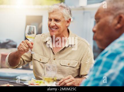 Smiling senior man raising a wineglass on a vineyard with friends. Happy caucasian man sitting and bonding during a wine tasting on a farm over the Stock Photo