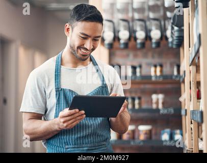 one young hispanic waiter using a digital tablet device while working in a store or cafe. Happy man checking inventory and stock of products while Stock Photo