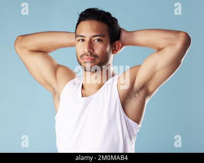 Handsome young hispanic man posing in studio isolated against a blue background. Mixed race male athlete wearing a vest and looking confident, healthy Stock Photo