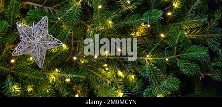 Christmas star on Xmas fir tree and bokeh lights background, copy space. Winter holiday decoration, card template, banner. Stock Photo